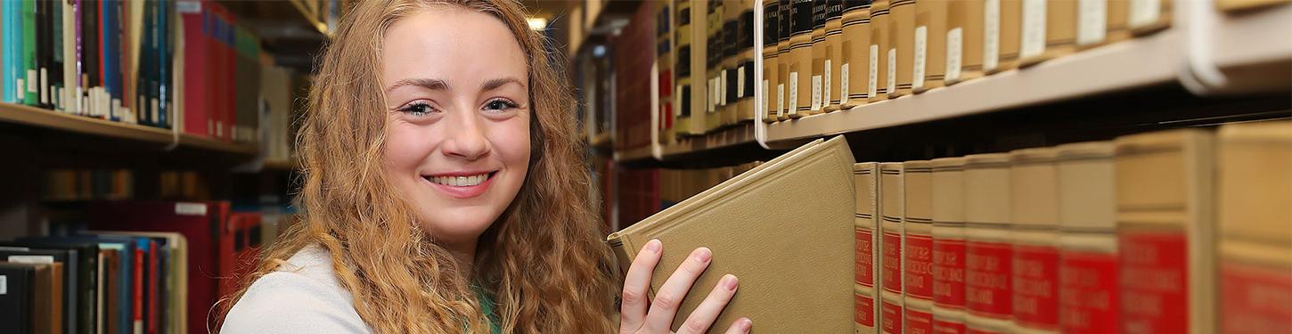 体育菠菜大平台 student takes a book of a library shelf